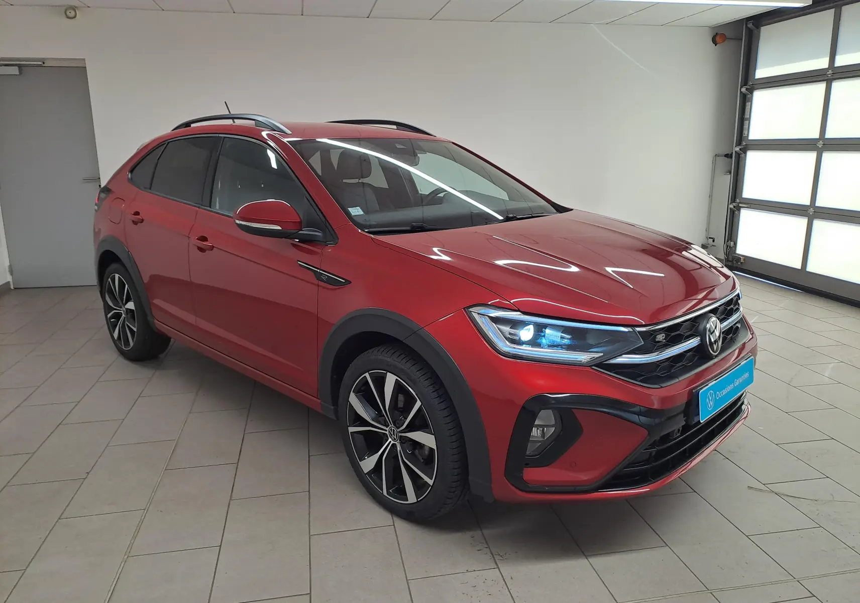 Volkswagen Taigo 1.5 TSI R-Line rouge Roi en 3/4 avant droit, jantes noires brillantes et phares allumés.
