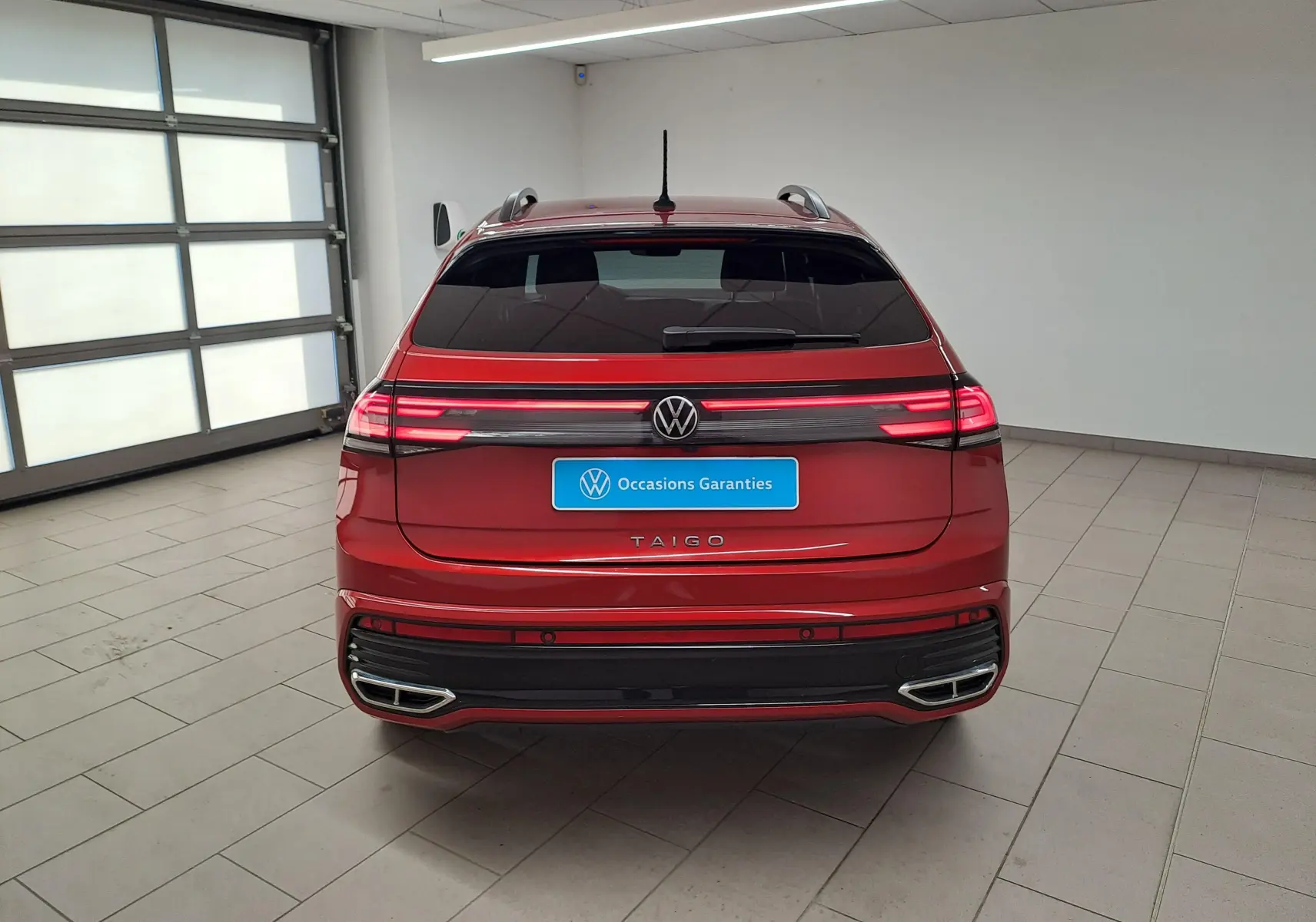 Vue arrière d'un Volkswagen Taigo 1.5 TSI 150 DSG7 R-LINE rouge Roi avec feux LED allumés dans un garage.