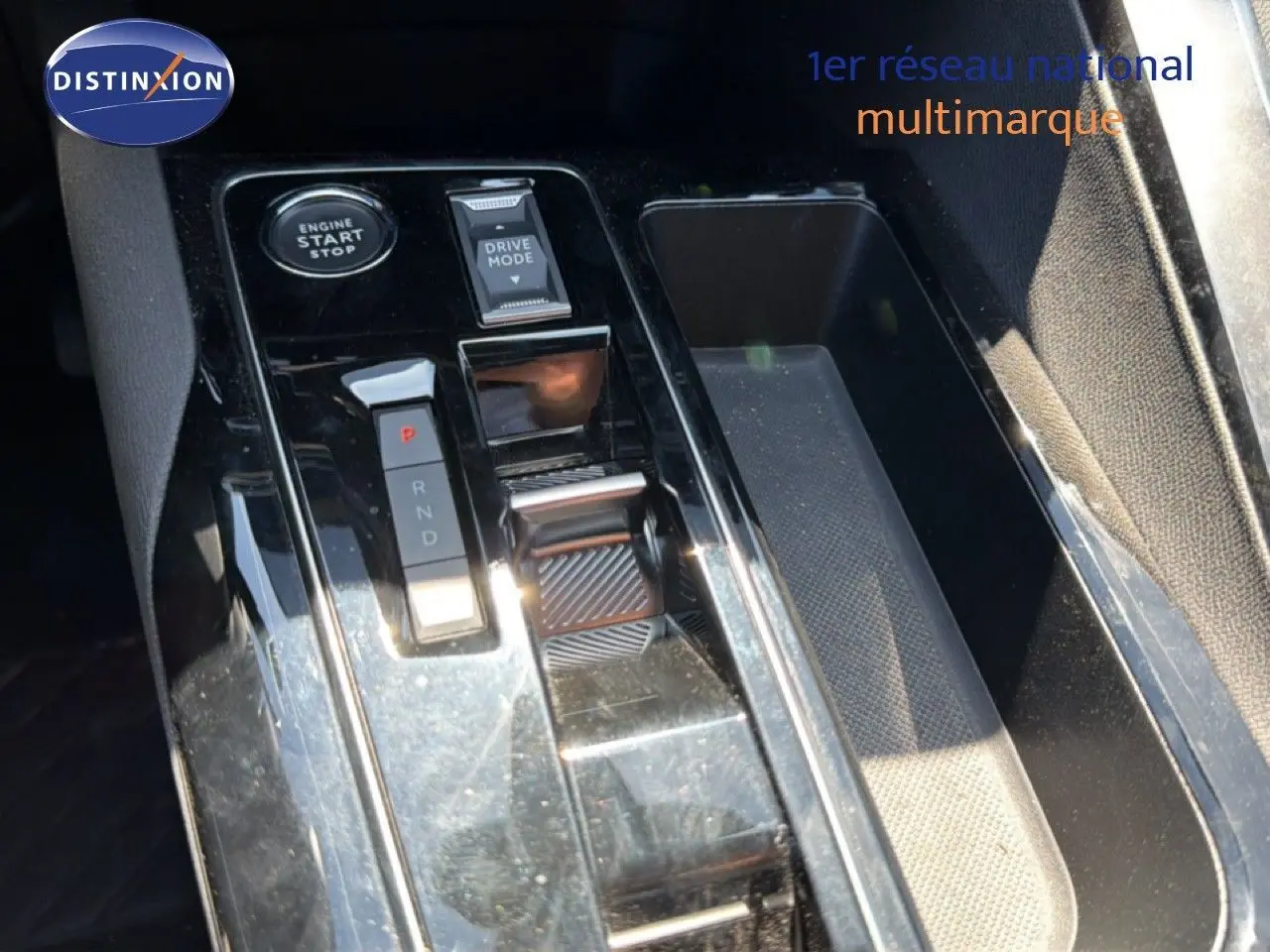 Gros plan sur la console centrale noire brillante du Peugeot 3008 Hybrid 2024 avec sélecteur de boîte auto et bouton Start/Stop.