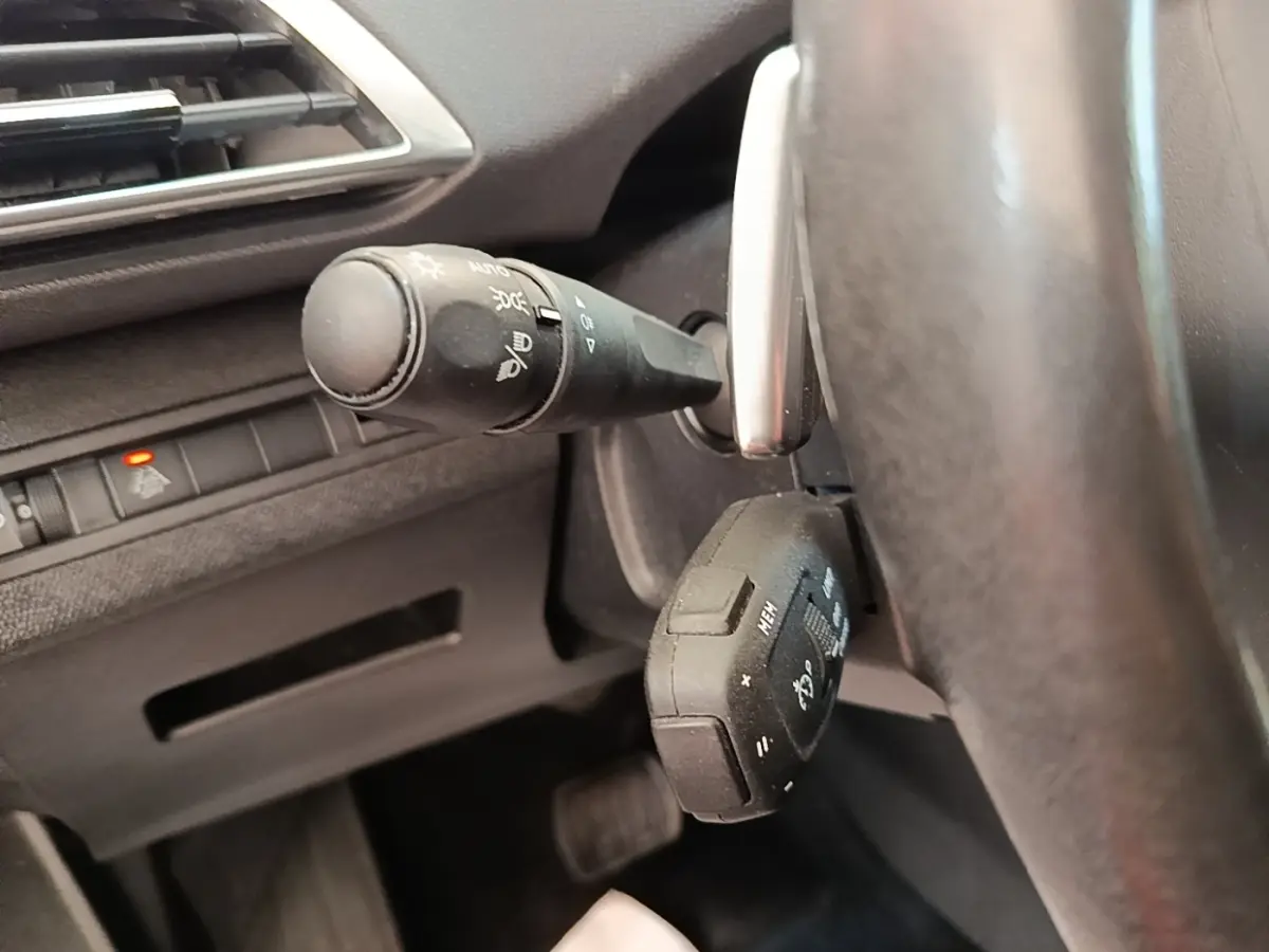 Gros plan sur la commande des feux et le volant cuir multi-fonctions du Peugeot 3008 gris foncé, côté gauche.