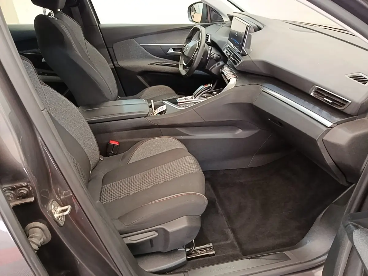 Vue intérieure côté passager avant du Peugeot 3008 gris foncé, montrant sièges tissu et tableau de bord moderne.