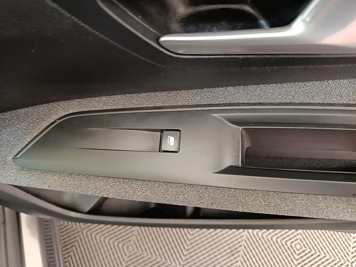 Gros plan sur la commande de lève-vitre côté conducteur du Peugeot 3008 gris foncé, intérieur tissu et plastique.