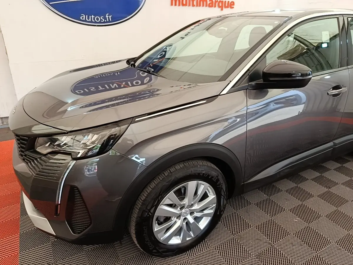 Vue 3/4 avant droit du Peugeot 3008 gris foncé avec phares LED et jantes alliage visibles en intérieur showroom.