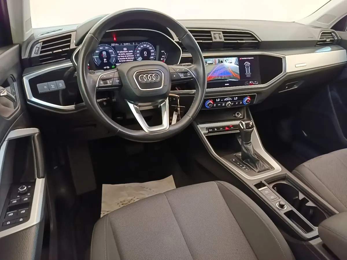 Intérieur Audi Q3 2023 vue avant du poste de conduite avec volant cuir noir et écran tactile central allumé.