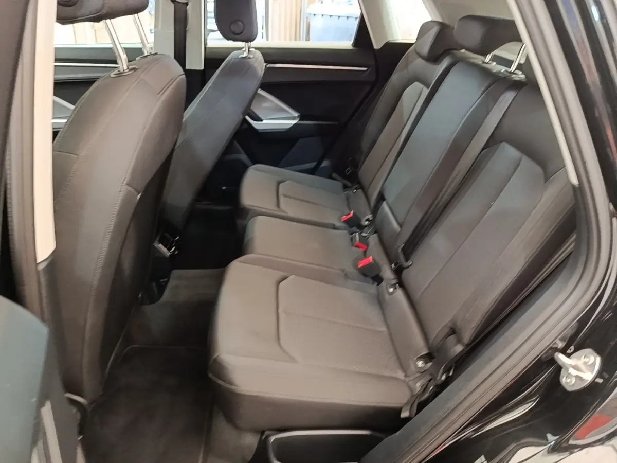 Vue latérale droite de l'habitacle arrière noir de l'Audi Q3 45 TFSI e 2023 avec sièges en tissu et ceintures de sécurité.