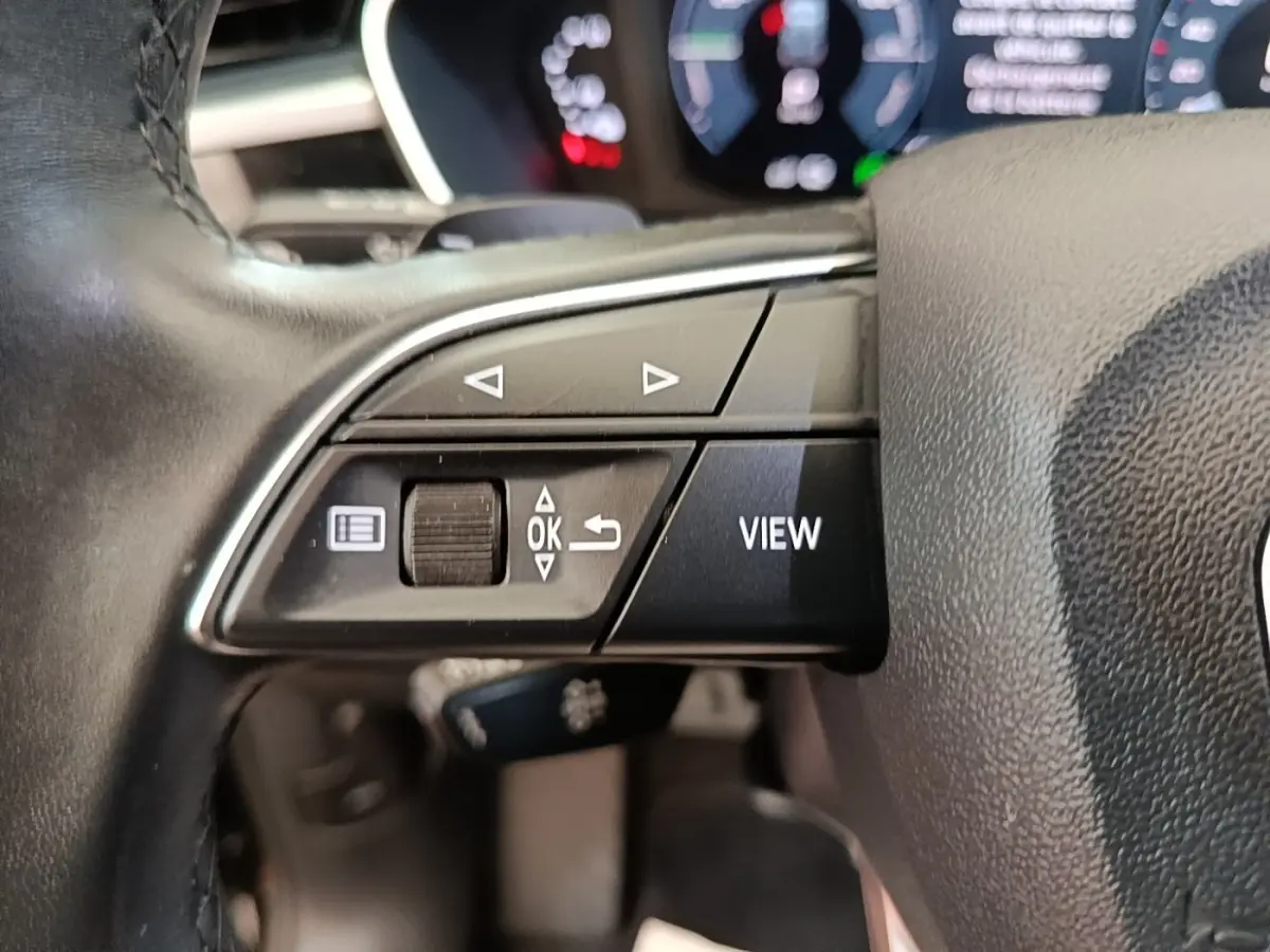 Gros plan sur le volant cuir noir multifonctions de l'Audi Q3 45 TFSI e avec commandes de navigation et bouton View.