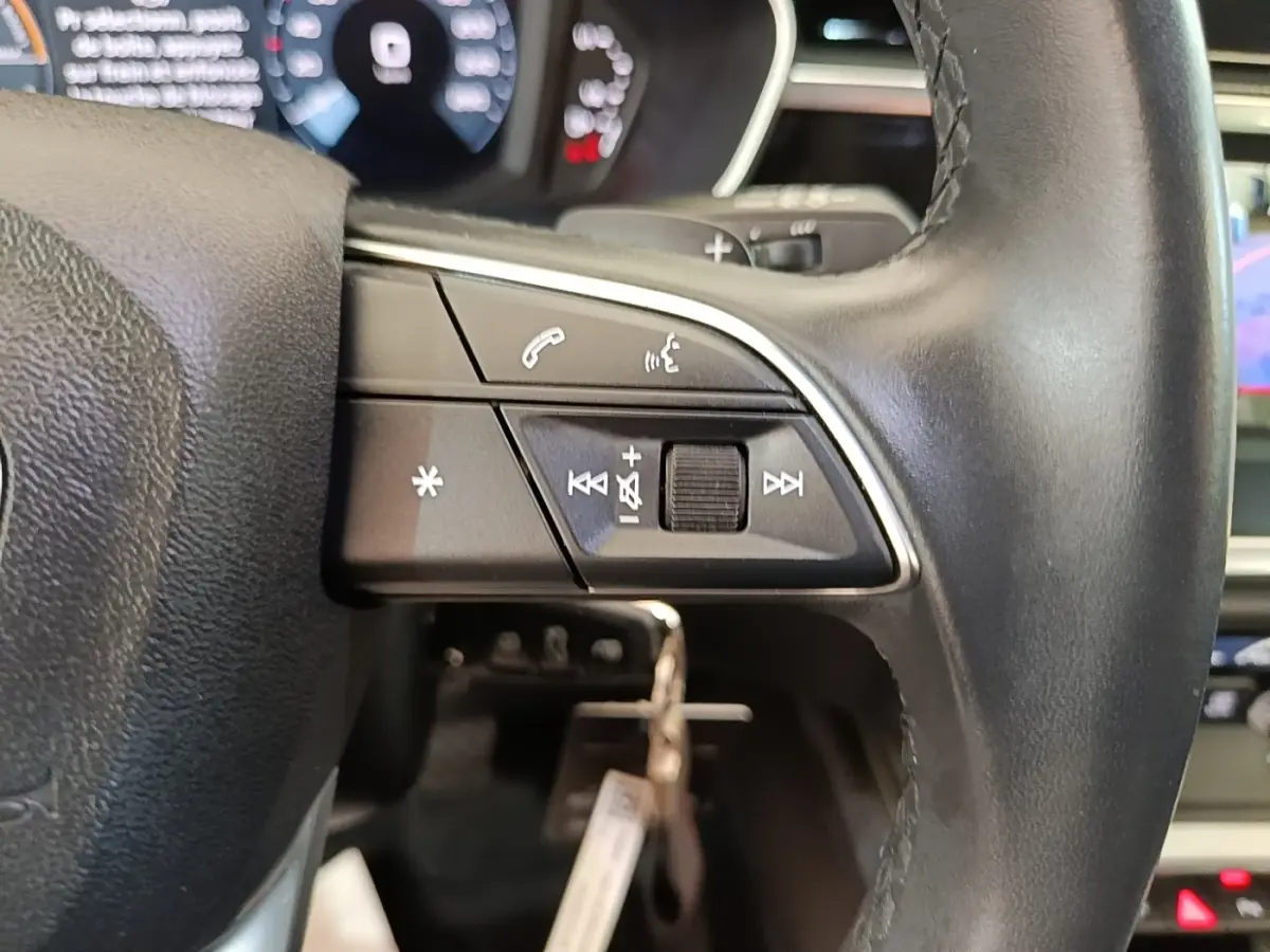 Gros plan sur le volant cuir multifonctions noir de l'Audi Q3 45 TFSI e avec commandes audio et téléphone.