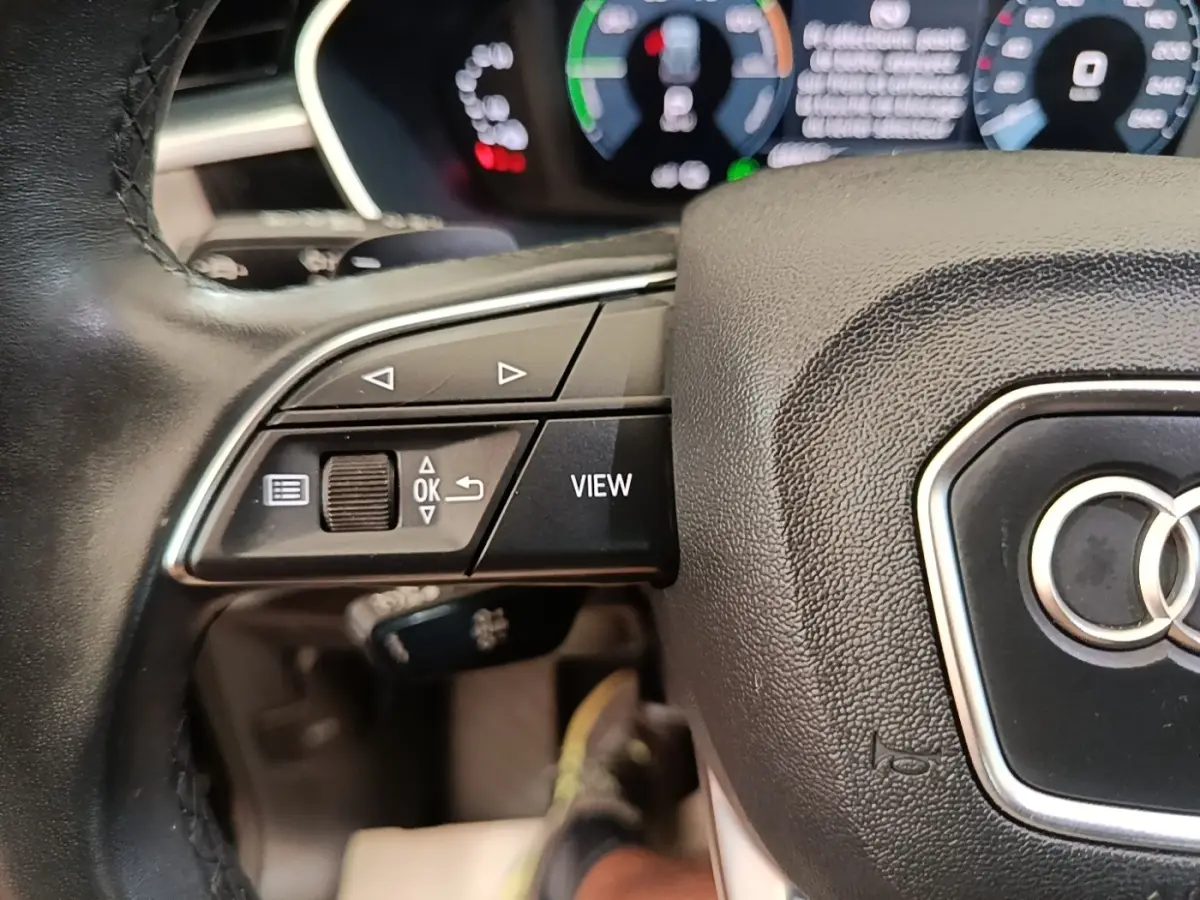 Gros plan sur le volant cuir multifonctions noir de l'Audi Q3 hybride rechargeable avec tableau de bord digital en arrière-plan.
