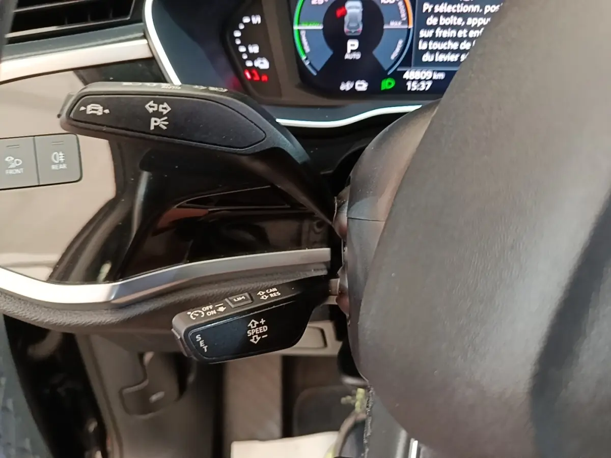Gros plan sur les commandes au volant cuir noir de l'Audi Q3 hybride rechargeable, avec tableau de bord digital en arrière-plan.