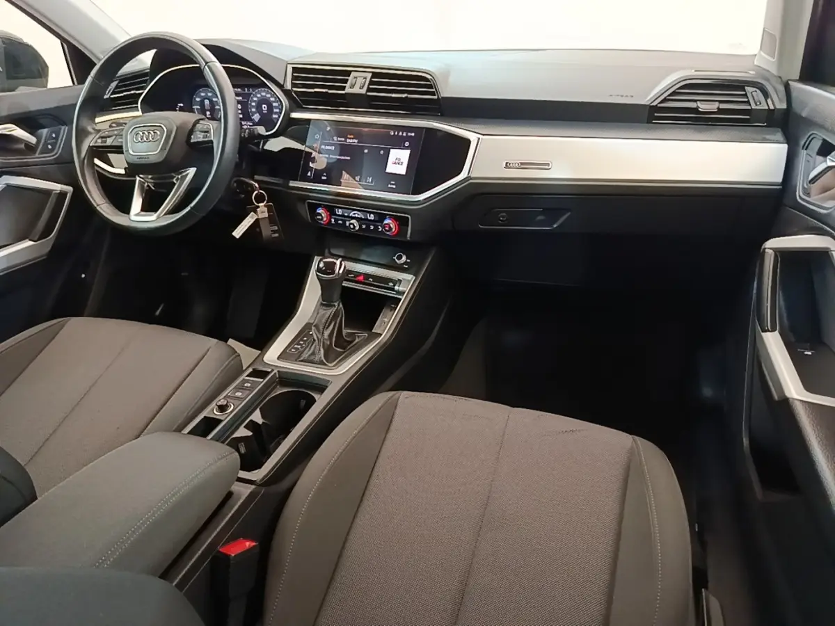 Vue intérieure avant droite de l'Audi Q3 45 TFSI E 2023 avec tableau de bord noir et écran tactile central.