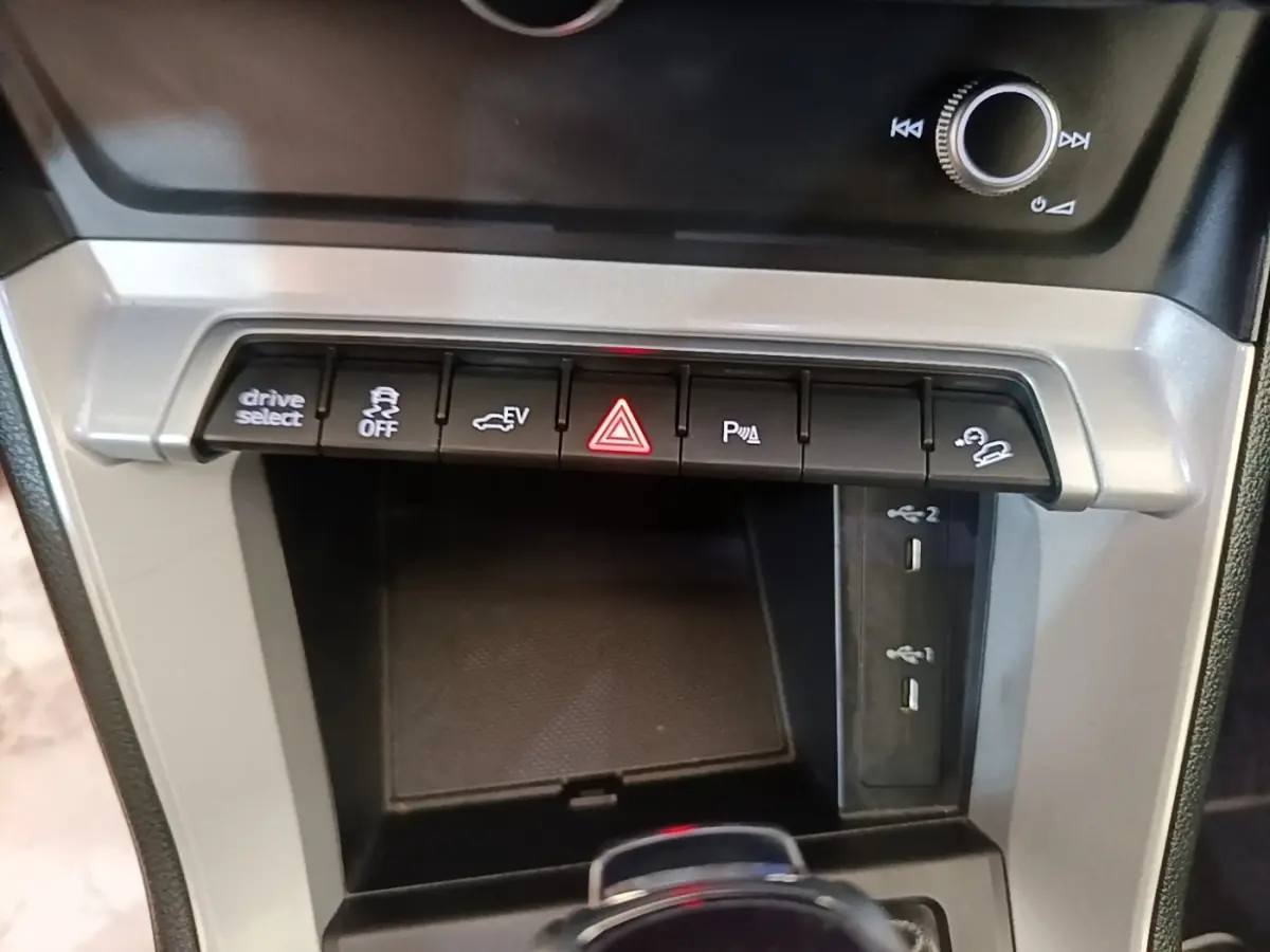 Gros plan sur la console centrale grise de l'Audi Q3 45 TFSI E avec boutons de contrôle et ports USB visibles.