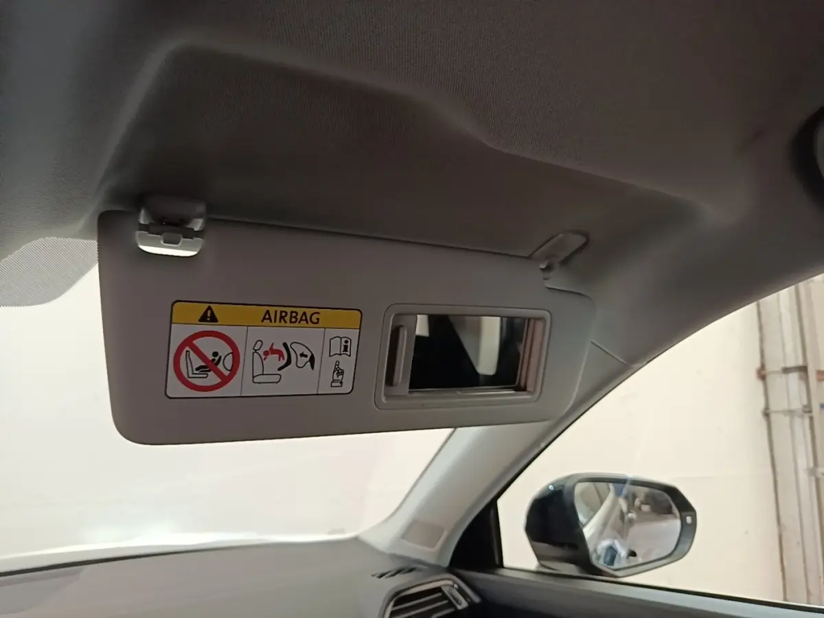 Détail intérieur du pare-soleil côté conducteur avec miroir et avertissement airbag, rétroviseur extérieur visible.