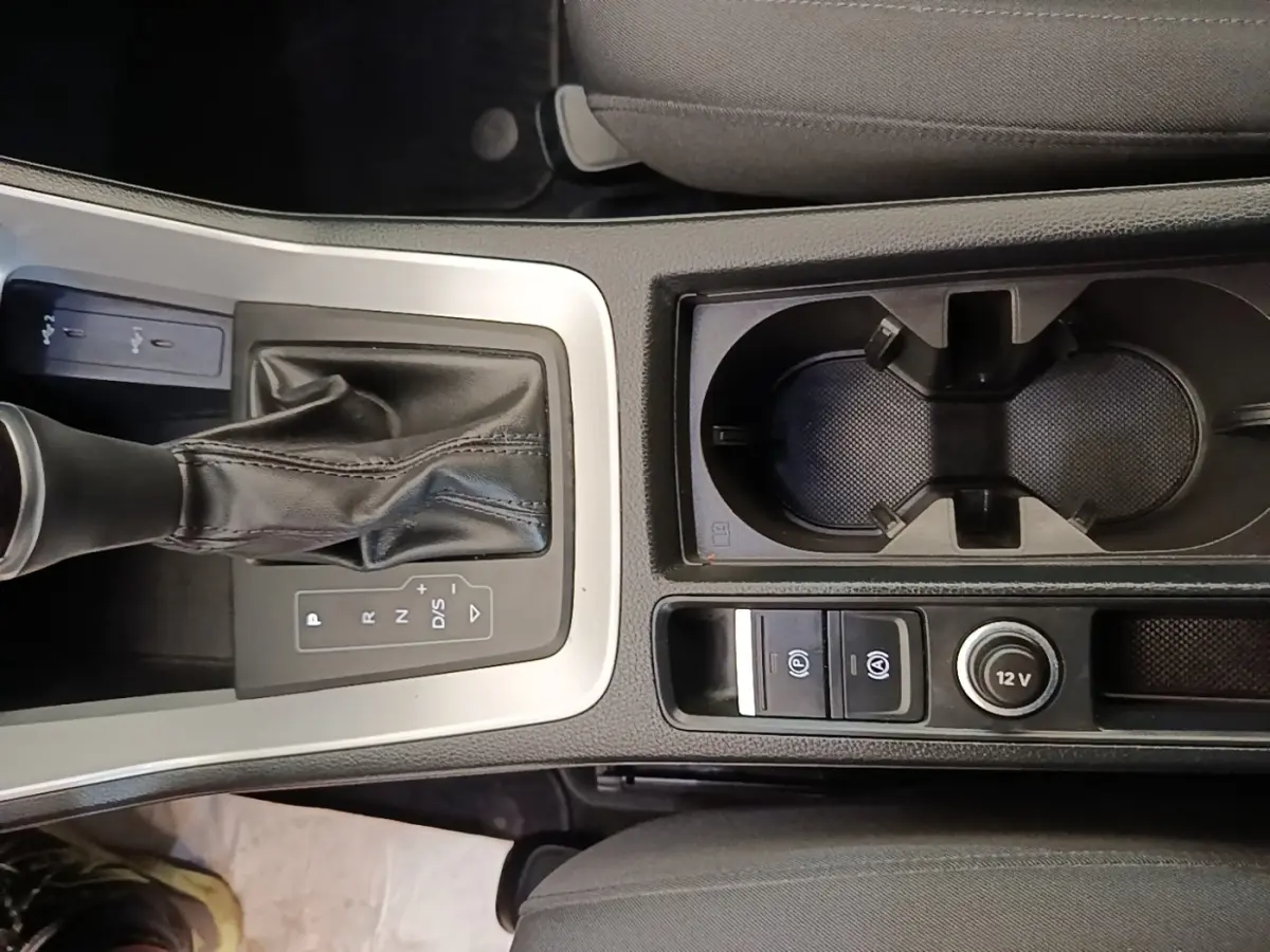 Vue plongeante sur la console centrale noire de l'Audi Q3 45 TFSI E avec levier de vitesses et porte-gobelets.
