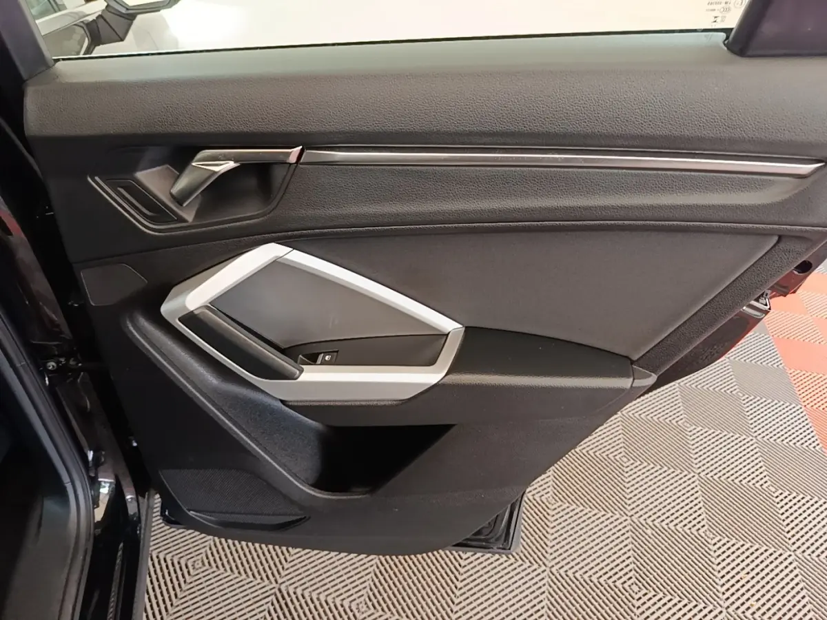 Vue rapprochée de la porte intérieure arrière gauche noire avec poignée argentée et commandes de vitre Audi Q3 2023.