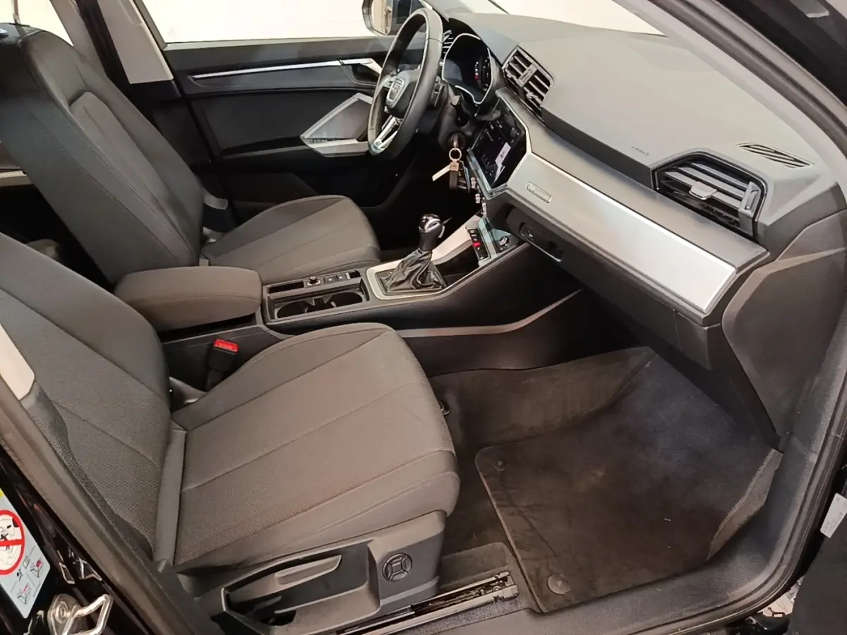 Intérieur avant droit de l'Audi Q3 45 TFSI e 2023 avec sièges gris, volant cuir multifonctions et tableau de bord moderne.