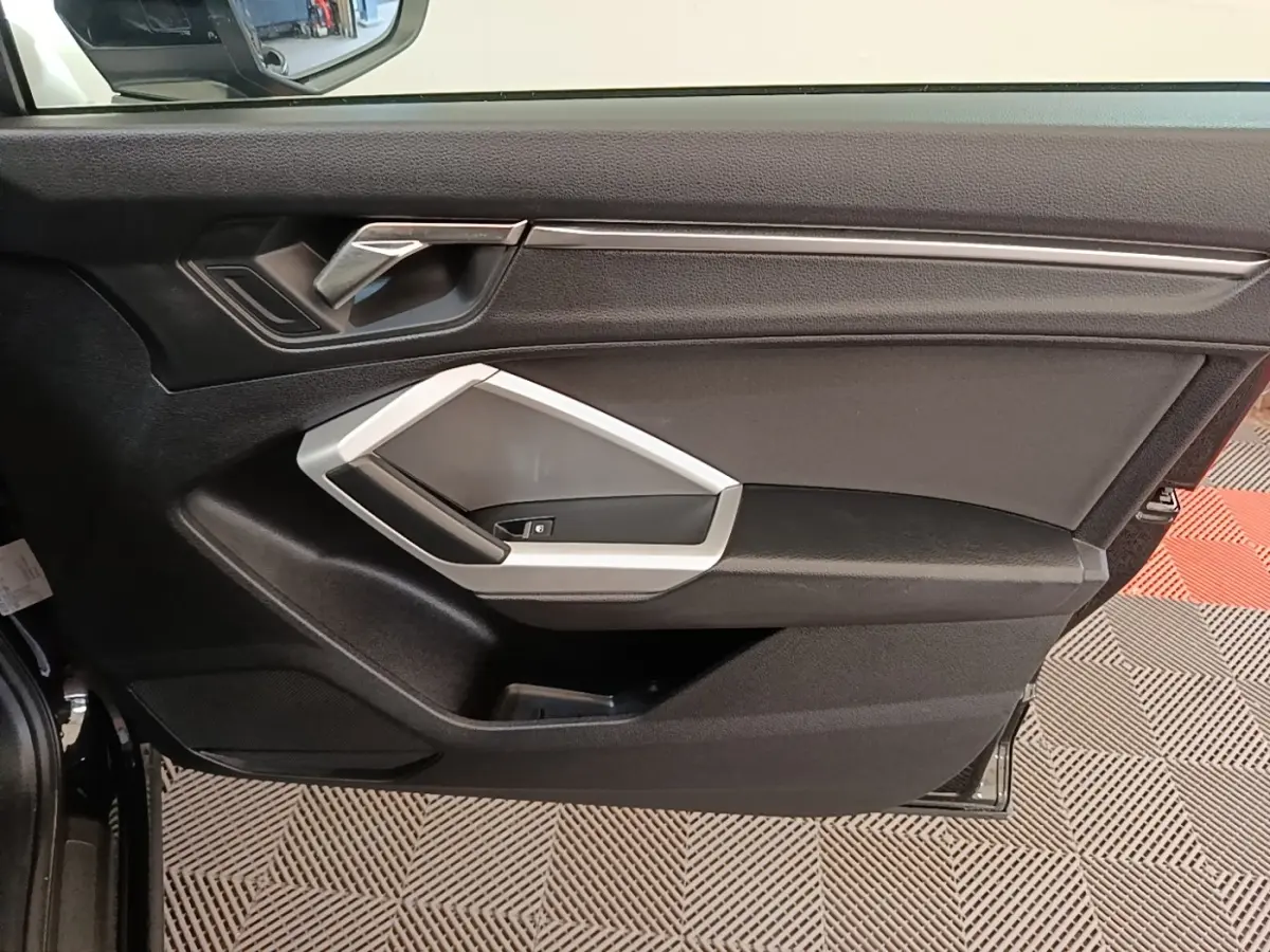 Vue intérieure côté gauche de la porte avant d’un Audi Q3 45 TFSI e 2023 avec garniture noire et insert argenté.