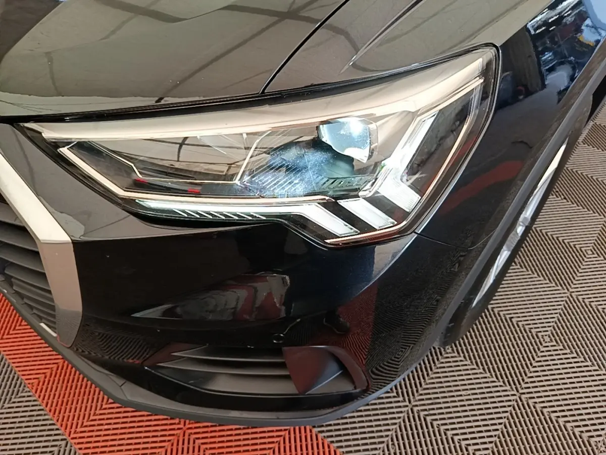 Gros plan sur le phare avant droit noir brillant de l’Audi Q3 45 TFSI e 2023 avec détails LED et calandre partielle.