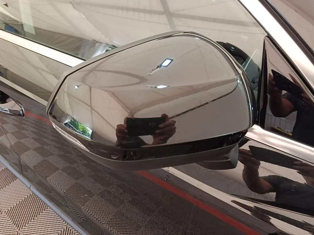 Rétroviseur côté gauche noir brillant d’un Audi Q3 hybride rechargeable 2023, reflet de l’environnement intérieur visible.