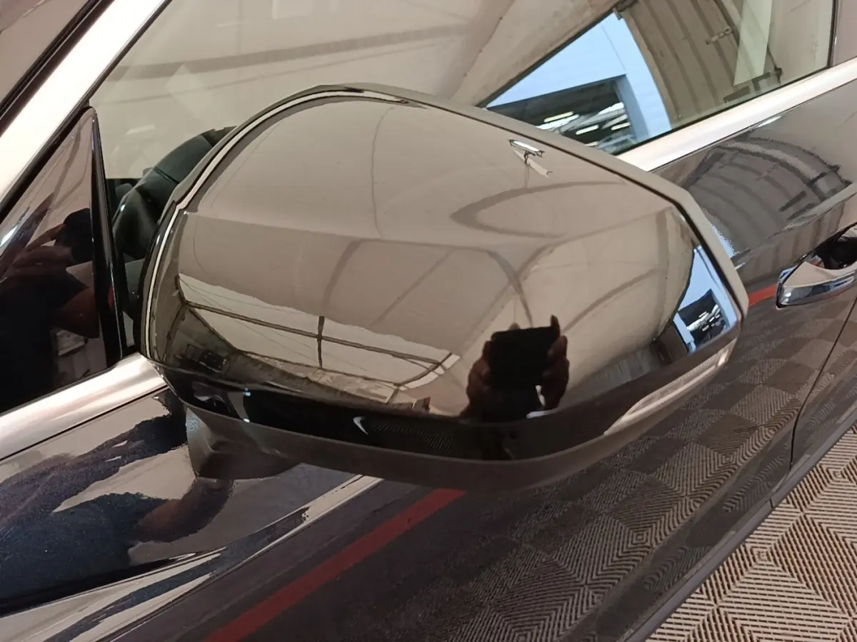 Rétroviseur droit noir brillant d’un Audi Q3 hybride rechargeable 2023, avec carrosserie sombre et poignée visible.