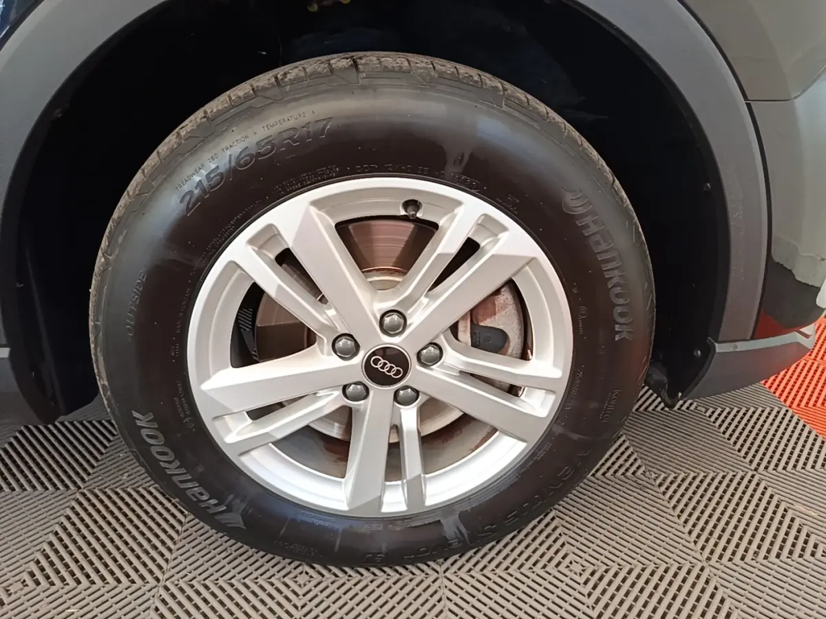 Gros plan sur la roue avant droite d'un Audi Q3 45 TFSI E 245 gris avec jante alliage et logo Audi central.