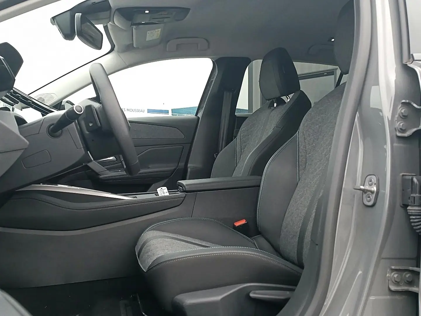 Vue intérieure côté conducteur de la Peugeot 408 Hybrid 145 allure gris sellenium avec sièges bi-matière et accoudoir central.