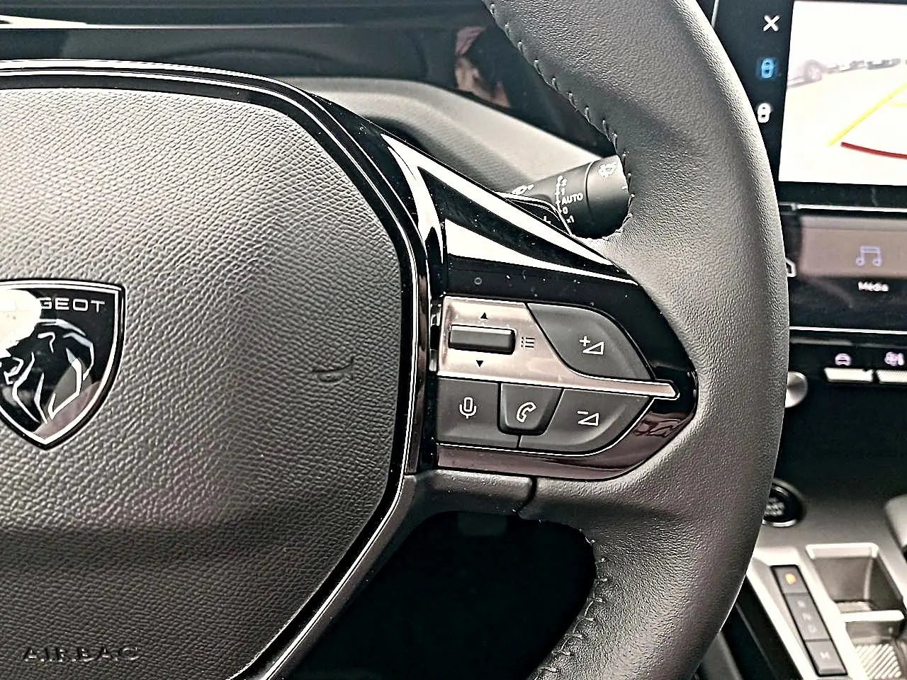 Gros plan sur le volant cuir noir de la Peugeot 408 Hybrid 145 allure, avec commandes multifonctions et logo lion central.