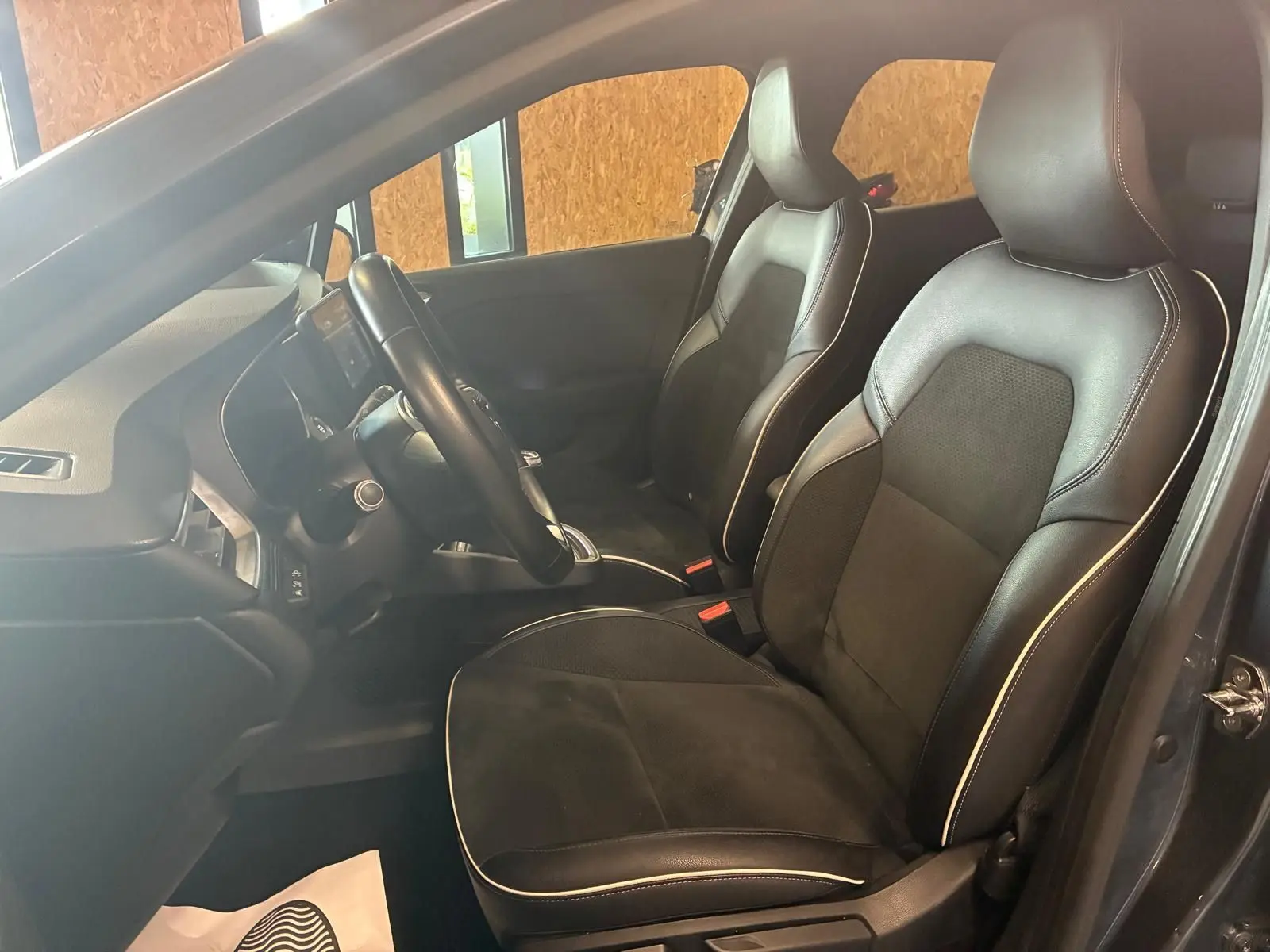 Vue intérieure côté conducteur de la Renault Clio gris 2020, sièges tissu noir avec surpiqûres blanches et volant multifonction.