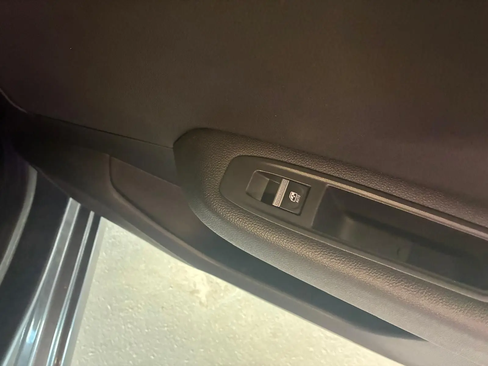 Gros plan sur le bouton de commande de la vitre électrique côté gauche dans une Renault Clio gris foncé, version 2020.