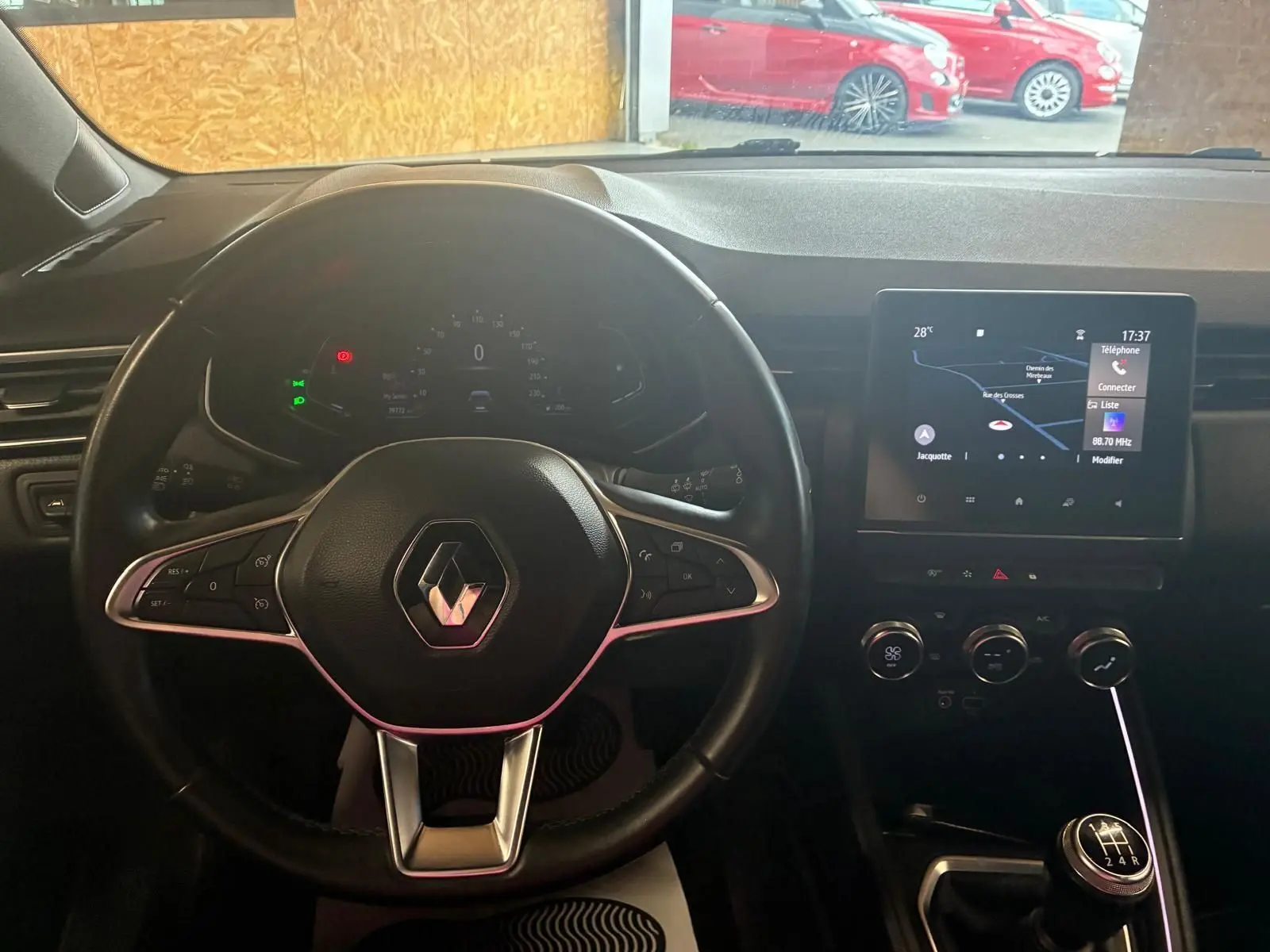 Vue intérieure centrée sur le volant Renault d'une Clio gris, avec tableau de bord numérique et écran tactile GPS.