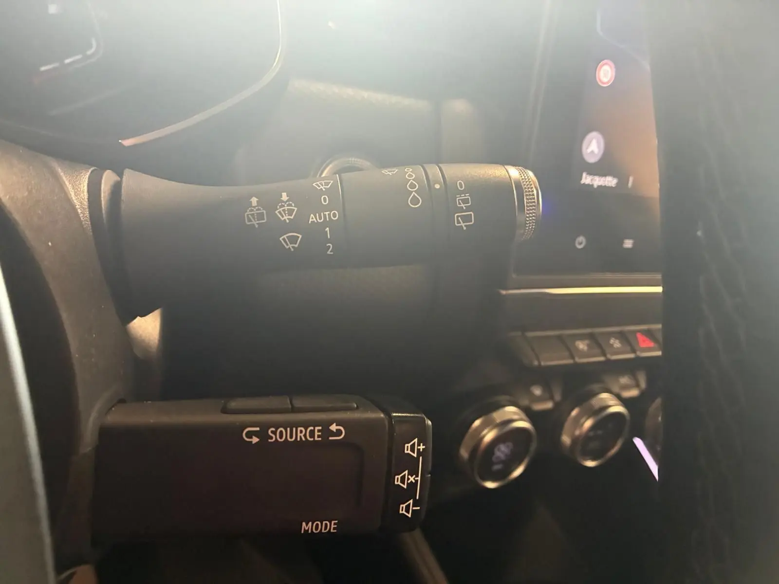 Gros plan sur les commandes au volant d'une Renault Clio gris 2020, avec boutons source et essuie-glace visibles.