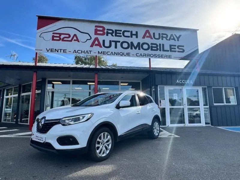 Renault Kadjar blanc en 3/4 avant droit devant un garage Brech Auray Automobiles par temps ensoleillé.