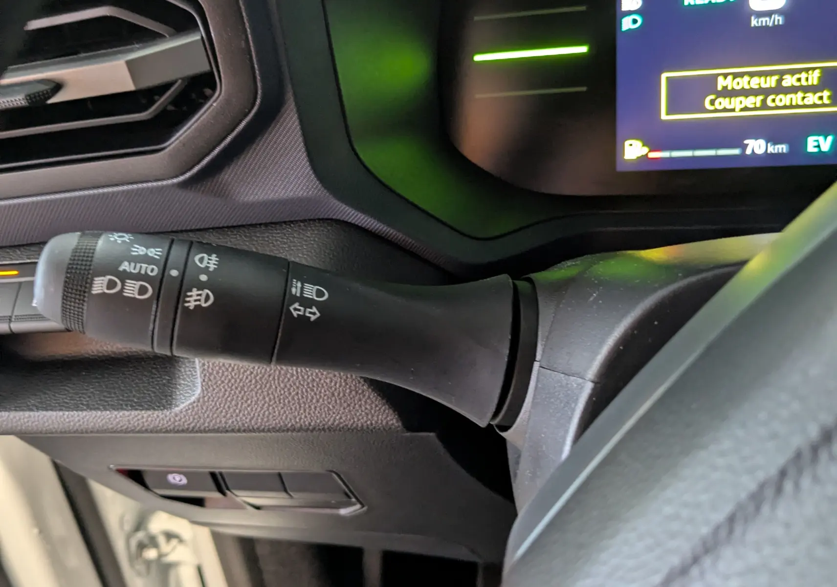 Gros plan sur la commande des phares à gauche du volant du Dacia Duster blanc glacier, tableau de bord numérique visible.