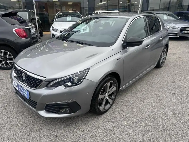 Peugeot 308 gris métal vue 3/4 avant droit, finition GT Line avec jantes alliage distinctives, stationnée en extérieur.