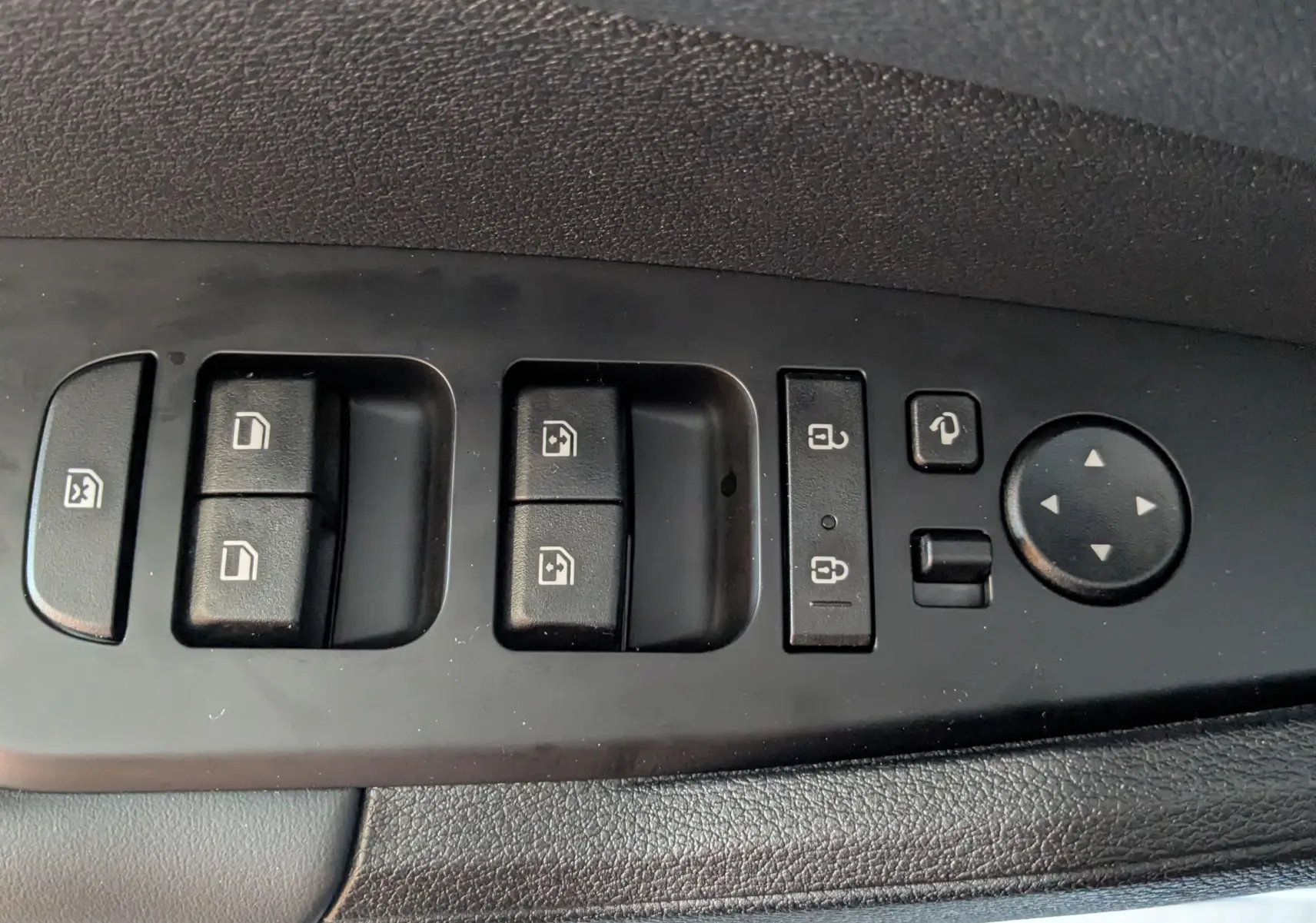 Gros plan sur les commandes de lève-vitres et rétroviseurs du côté gauche intérieur d’un Kia Sportage blanc.
