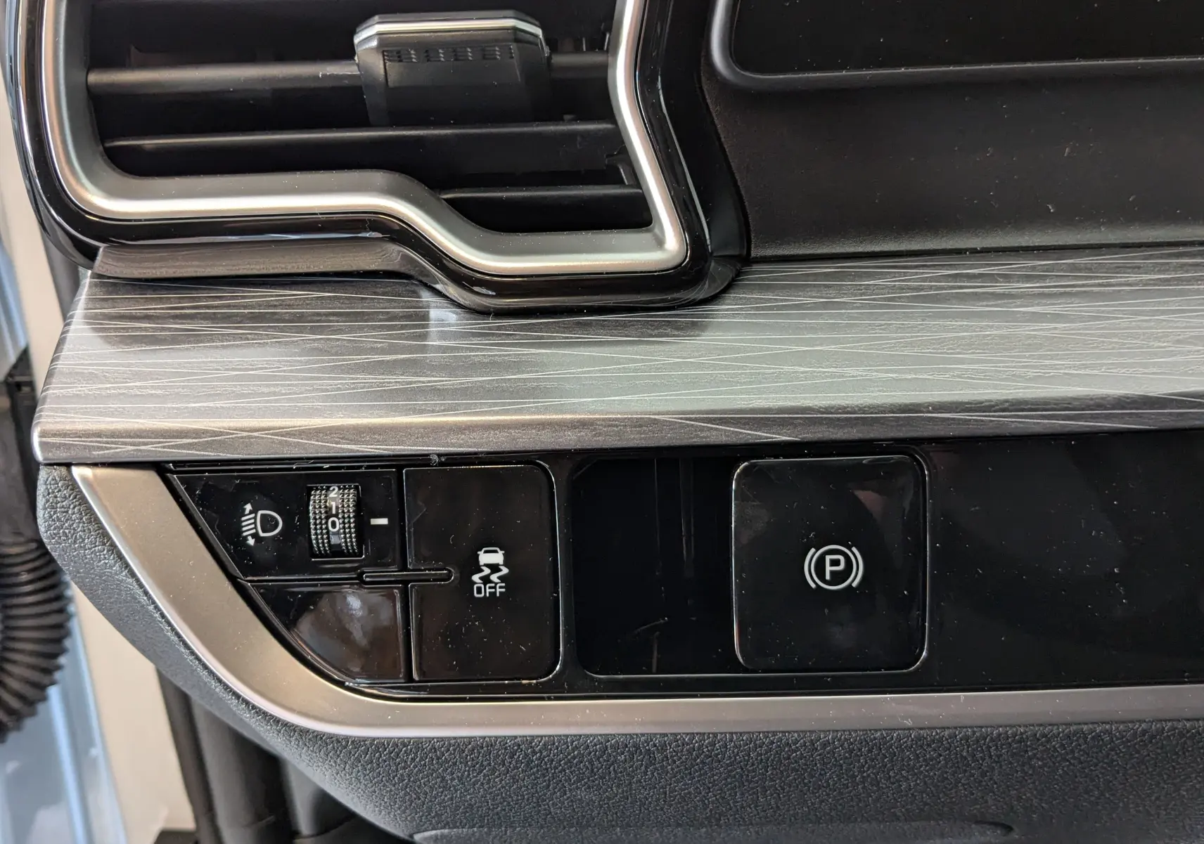 Détail du tableau de bord noir et gris avec commandes d'éclairage et frein à main électrique sur KIA SPORTAGE 2025.