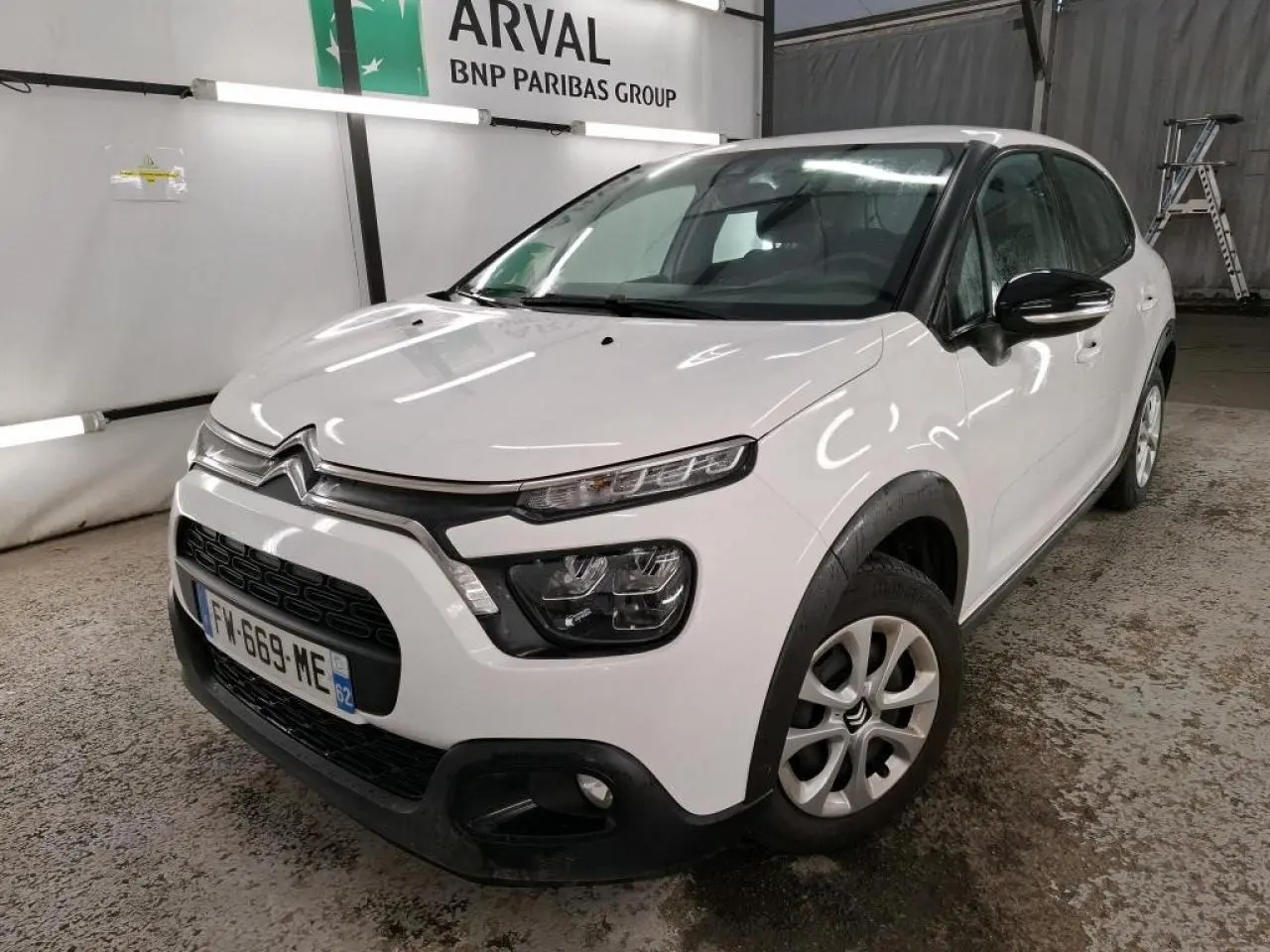 Vue 3/4 avant droite d'une Citroën C3 blanche avec coques de rétroviseurs noires et jantes 15 pouces en intérieur industriel.