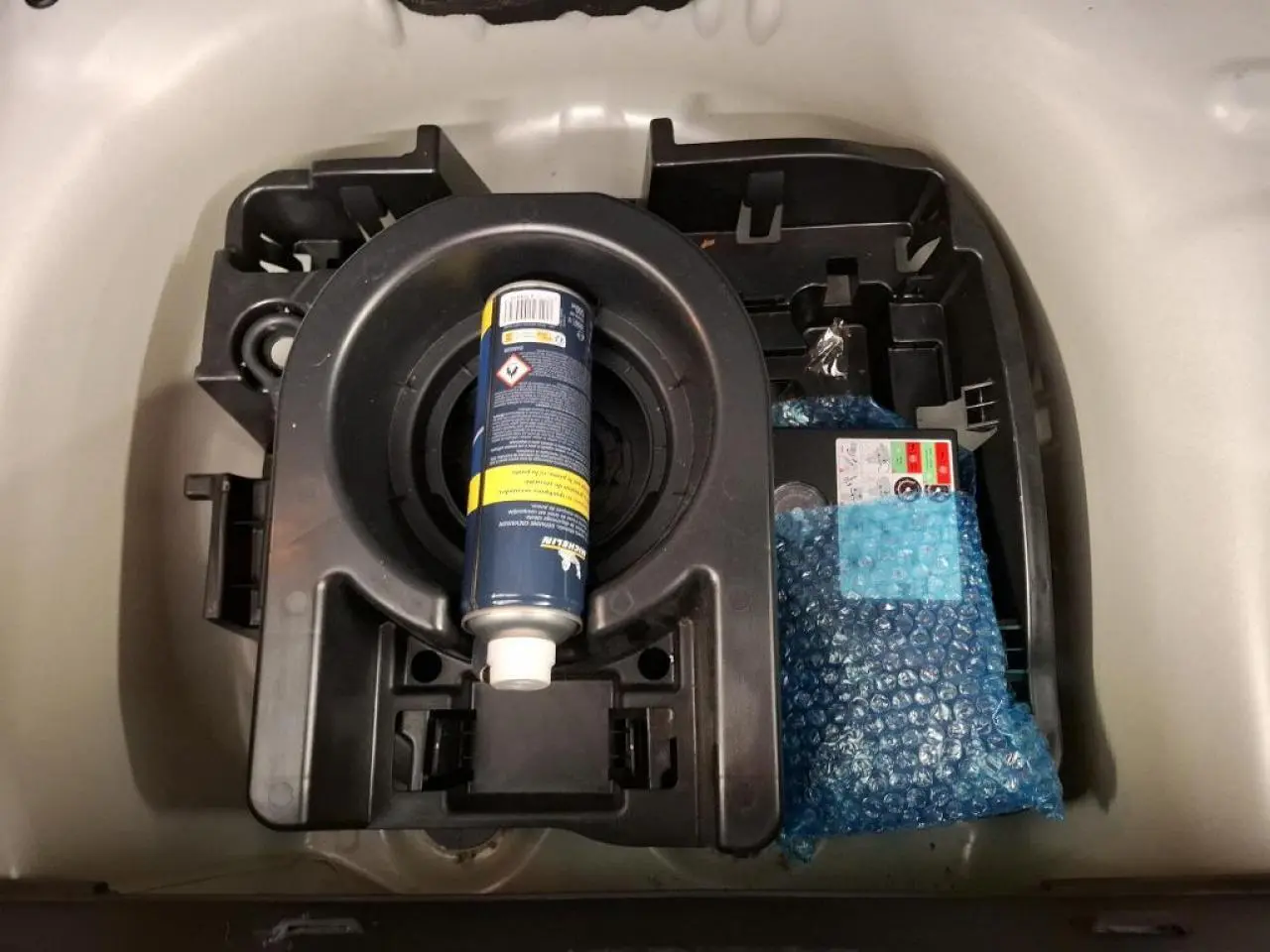 Vue rapprochée du coffre d'une Citroën C3 blanche montrant le kit de dépannage avec bombe anti-crevaison.
