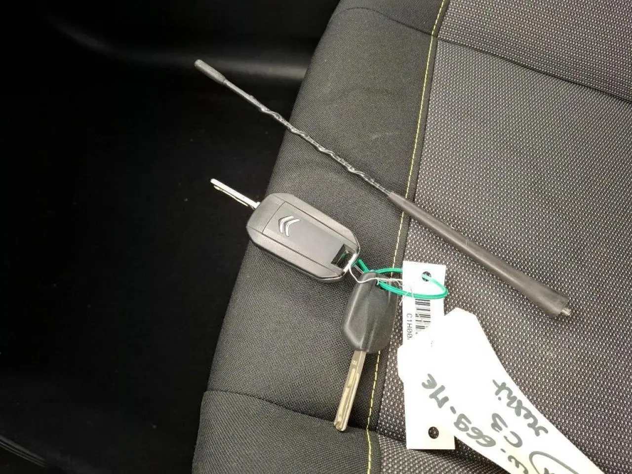 Clé et télécommande Citroën posées sur siège tissu gris foncé avec surpiqûres jaunes, intérieur Citroën C3 2021.