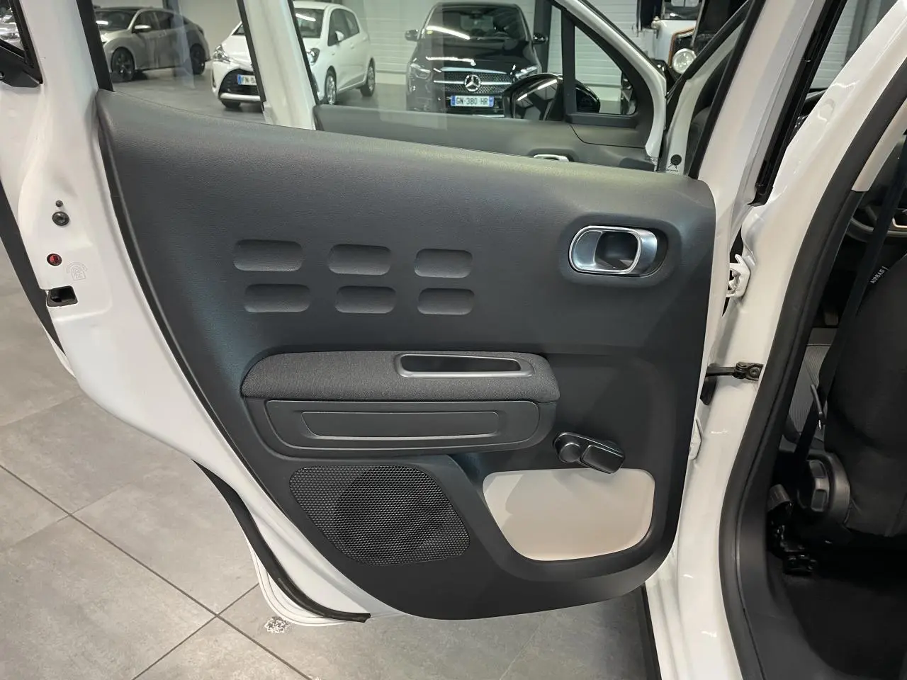 Vue intérieure sur la porte arrière gauche blanche d'une Citroën C3 2021 avec poignée et manivelle de vitre noire.