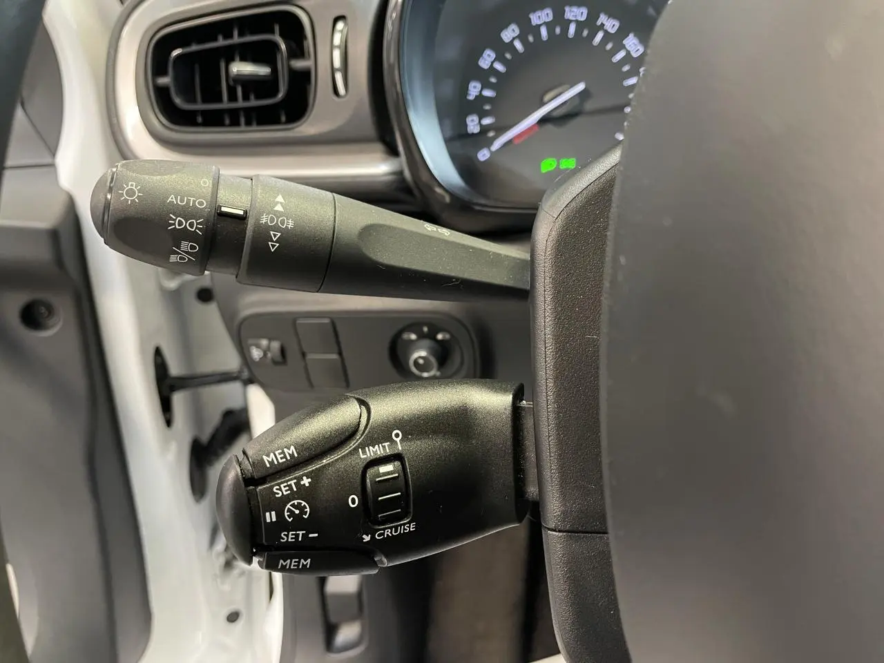 Gros plan sur les commandes au volant côté gauche de la Citroën C3 blanche, avec levier de clignotants et régulateur de vitesse.