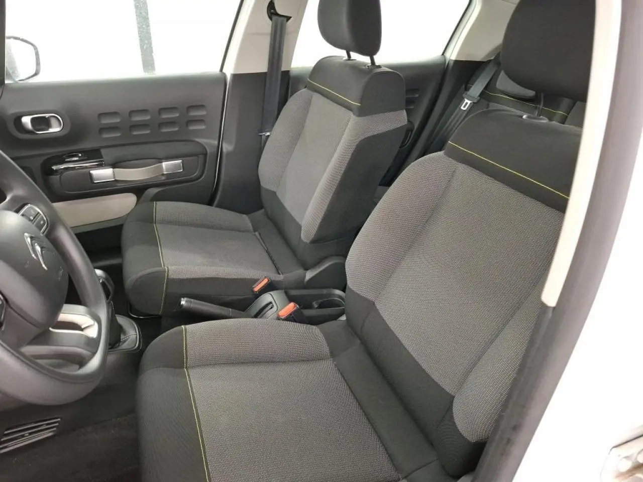 Vue intérieure côté gauche de la Citroën C3 blanche, montrant les sièges avant gris à surpiqûres jaunes et la portière.