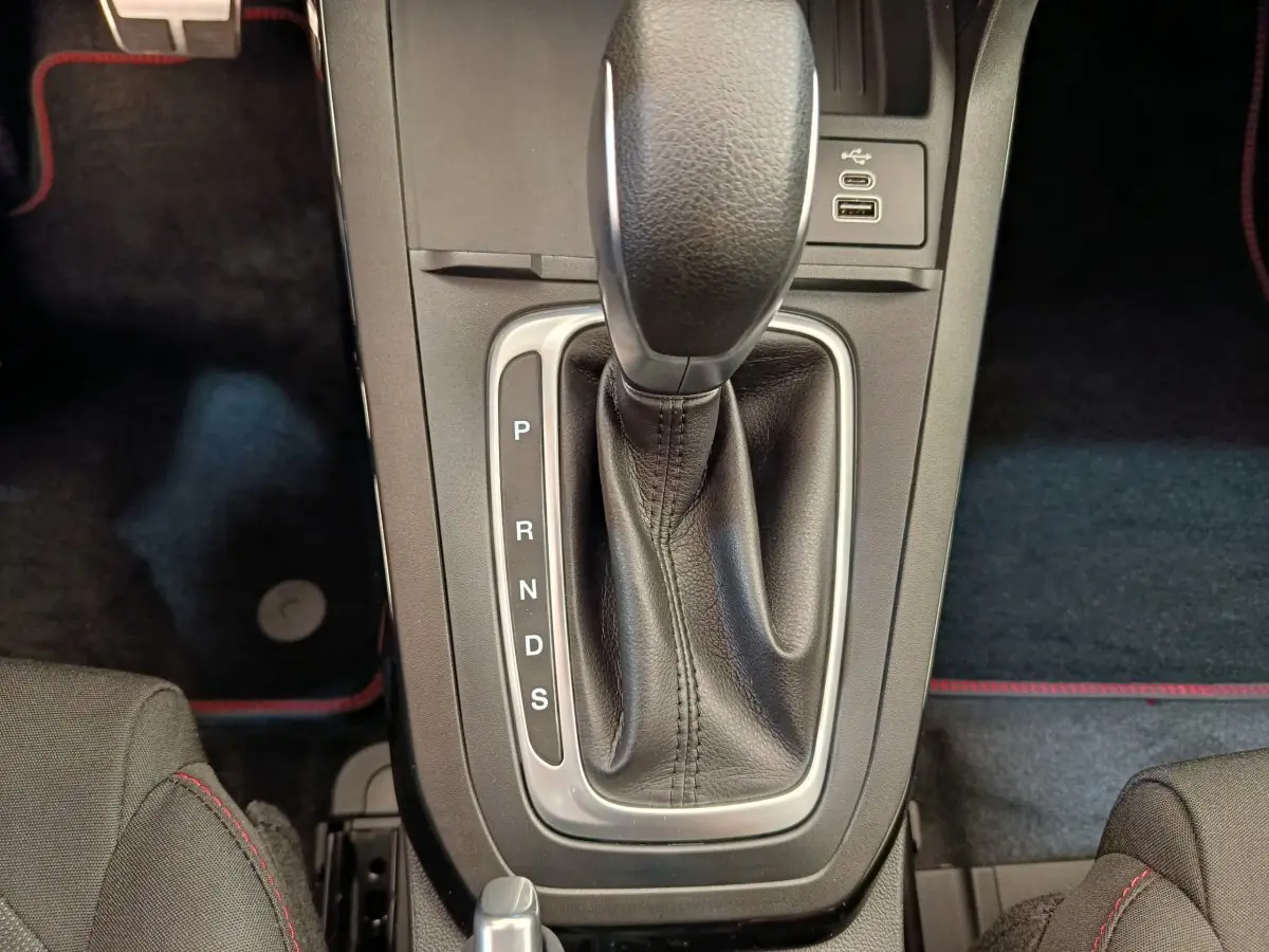 Gros plan sur la console centrale de la Ford Puma bleue, montrant le levier de vitesses automatique en cuir noir avec surpiqûres rouges.