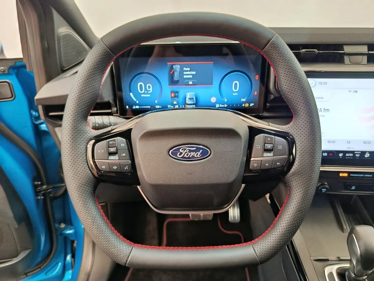 Vue centrée sur le volant cuir noir avec surpiqûres rouges du Ford Puma bleu, tableau de bord numérique et écran tactile visibles.