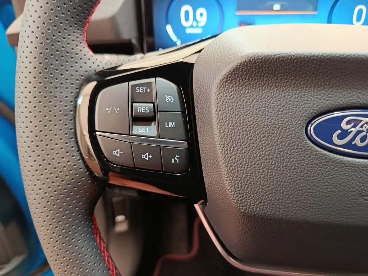 Gros plan sur le volant cuir noir perforé avec commandes multifonctions à gauche du Ford Puma bleu.