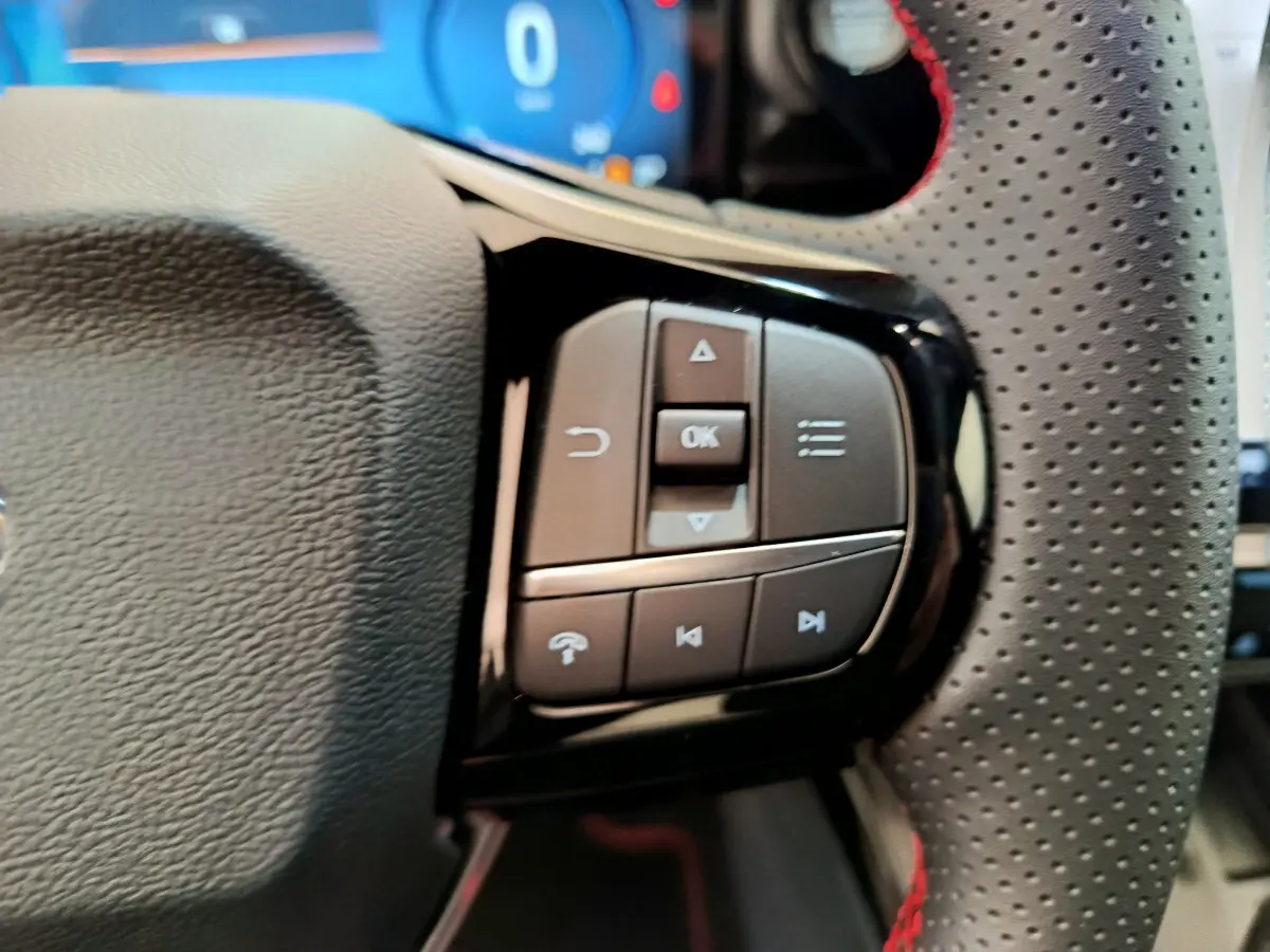 Gros plan sur les commandes multifonctions noires à droite du volant perforé avec surpiqûres rouges du Ford Puma bleu.