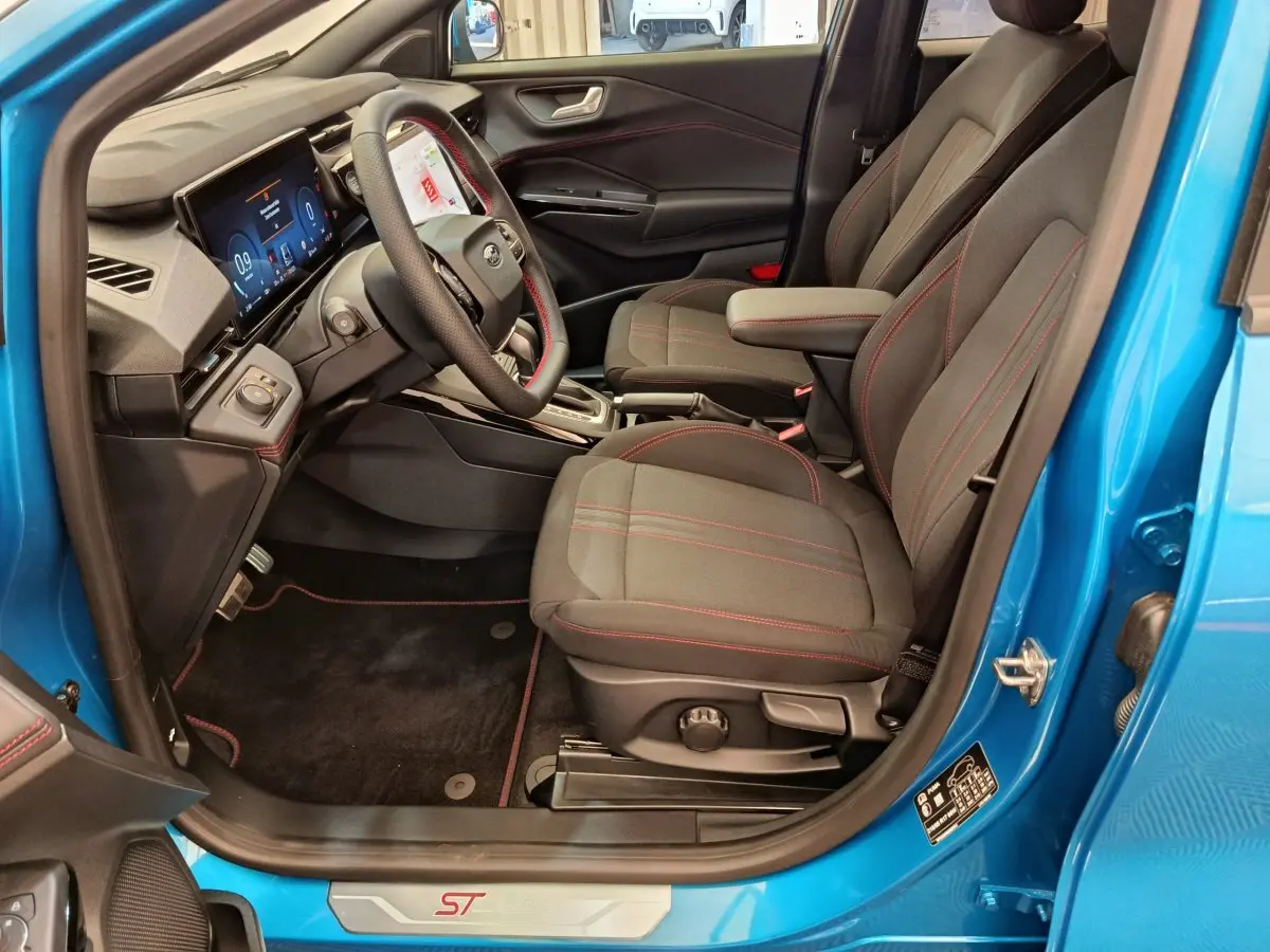 Vue intérieure côté conducteur du Ford Puma bleu 2025, sièges noirs avec surpiqûres rouges et tableau de bord numérique.