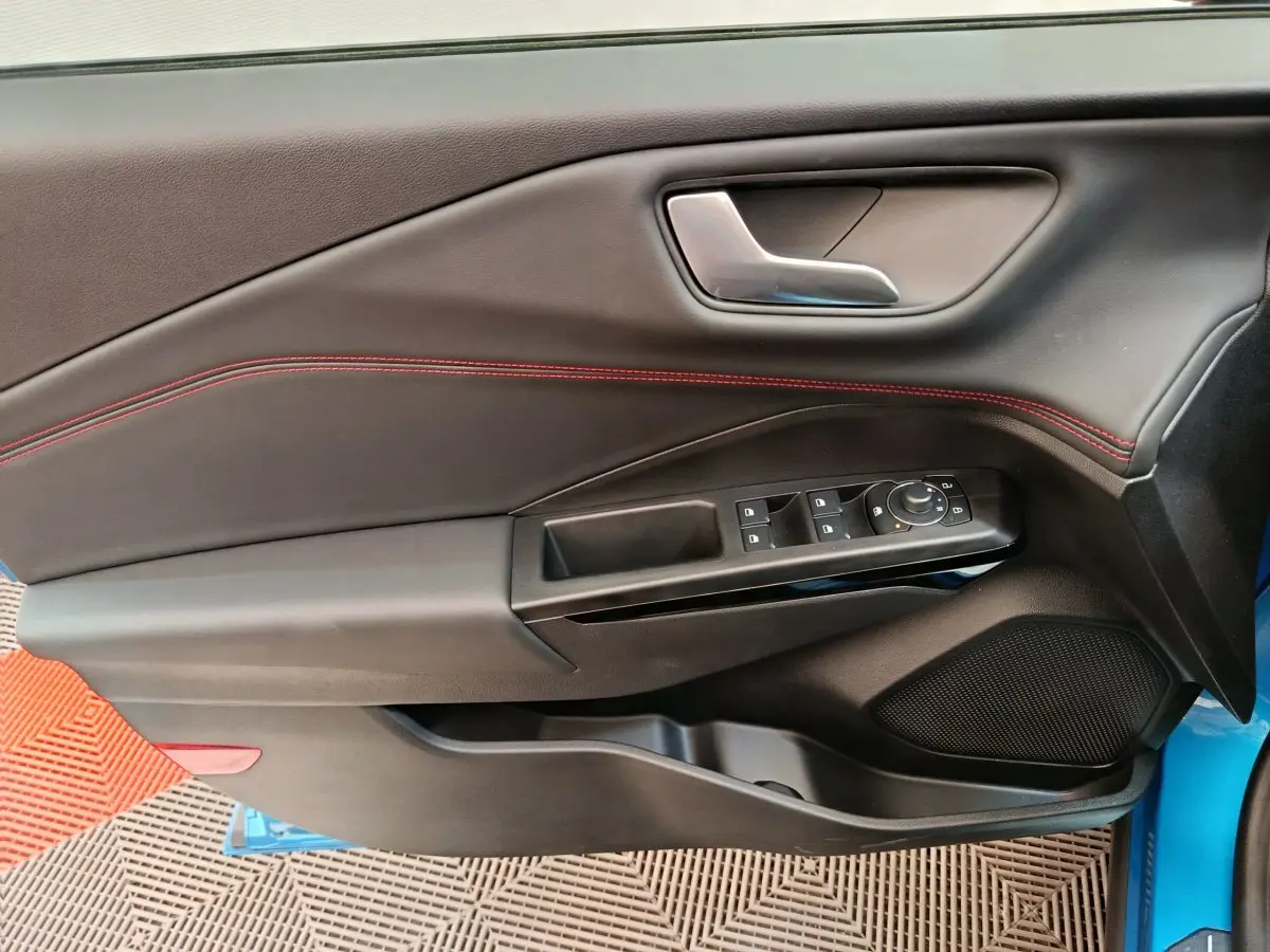 Vue intérieure côté gauche de la porte d’une Ford Puma bleue avec surpiqûres rouges et commandes électriques.