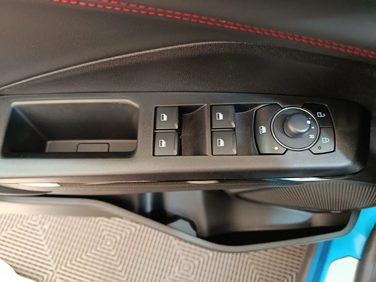 Vue rapprochée des commandes de lève-vitres et rétroviseurs sur la porte côté conducteur d’un Ford Puma bleu.