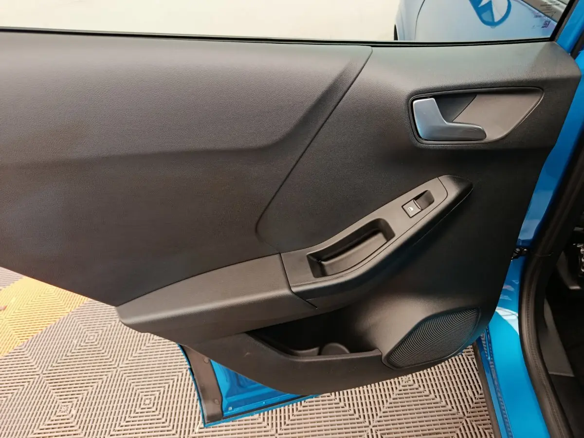 Vue intérieure de la porte avant gauche noire avec poignée et bouton de vitre, cadre bleu visible sur Ford Puma 2025.