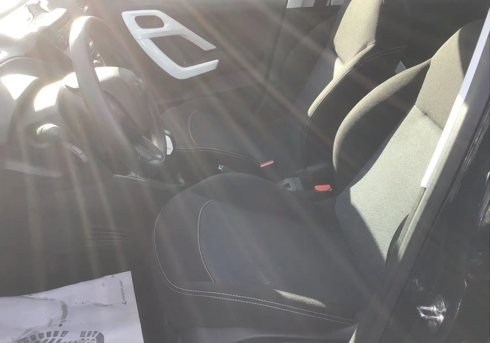 Intérieur de la Peugeot 208 essence 2018, vue côté conducteur, sièges noirs avec surpiqûres blanches, volant visible.